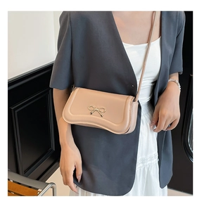Detail of a light pink bow-knot crossbody bag with gold hardware worn by a model