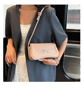 Close-up of a beige crossbody bag featuring a delicate gold bow and a knot-detailed strap