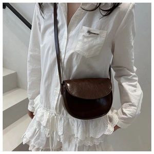 Detail view of dark brown gloss leather saddle bag with vintage flap on white stairs