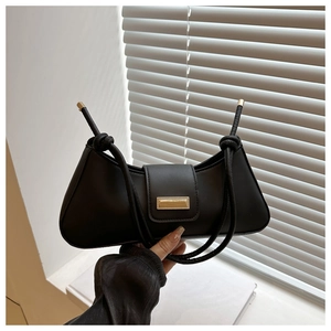 Close-up of black baguette bag with gold buckle and knotted rope shoulder strap detail