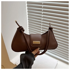 Close-up of brown half-moon baguette bag with knot strap and gold metal hardware