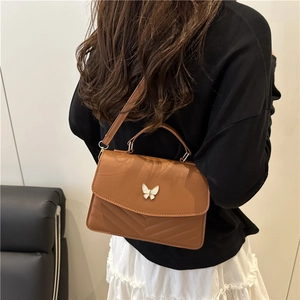 Brown quilted crossbody bag with gold butterfly clasp shown on model with shoulder strap