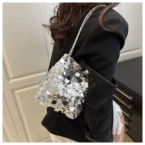Close-up of silver sequin bucket bag with metal chain strap worn on a black blazer