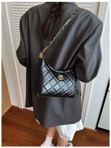 Detail of black quilted leather hobo bag with gold chain strap worn on the shoulder