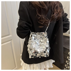 Silver sequin bucket bag with metal chain strap shown against a black blazer outfit