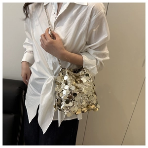 Detailed view of shimmering gold sequin bucket bag with metal chain strap worn by a model