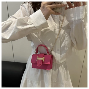 Detail of fuchsia mini crossbody bag with golden H buckle and chain strap on white dress