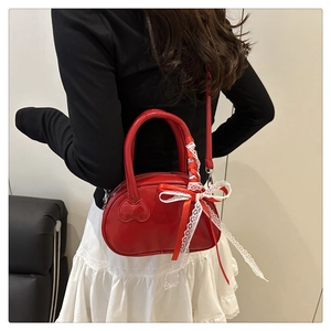 Detail of red glossy lacquer bag with white lace bow on the handle and thin shoulder strap