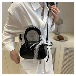 Minimalist black glossy handbag with bow details and lace ribbon on a warm white background