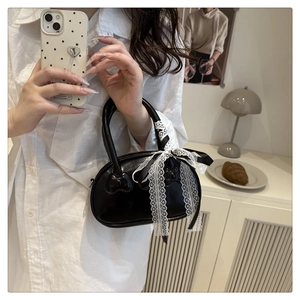 Detail of black glossy handbag with embossed heart and white lace bow decoration