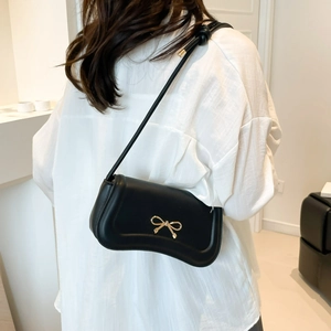 Minimalist black matte leather shoulder bag with a gold metal bow and knotted rope strap