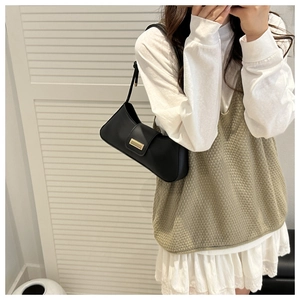 Detail of a chic black leather baguette bag with a sleek gold buckle on a model shoulder