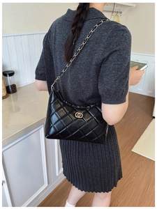 Gros plan du sac à bandoulière noir matelassé avec chaîne dorée porté par un mannequin