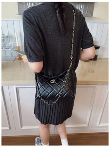 Détail d'un sac matelassé noir avec chaîne dorée porté par un mannequin dans une cuisine
