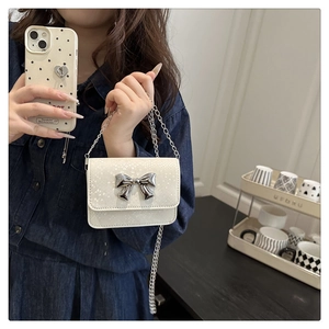 Detailed macro view of white snake-textured leather and silver metal bow on small crossbody bag