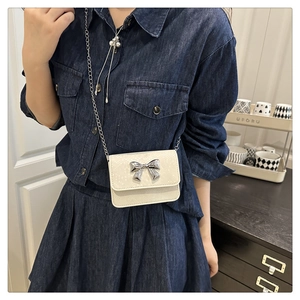 Detailed view of mini white crossbody bag with silver bow and metallic chain strap