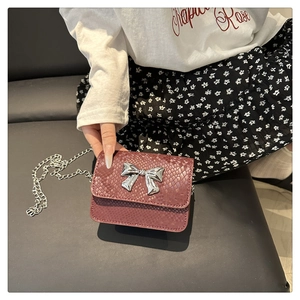 Detail of burgundy snakeskin crossbody bag with silver bow and chain strap on model