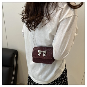 Detail of burgundy snakeskin crossbody bag with silver bow accent on model
