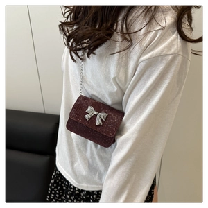 Detail of burgundy snakeskin crossbody bag with silver bow and metal chain strap