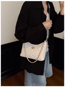 Détail d'un sac à bandoulière matelassé blanc avec chaîne dorée et logo en métal doré
