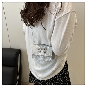 Mini silver snake-embossed crossbody bag with metal bow detail shown on a model