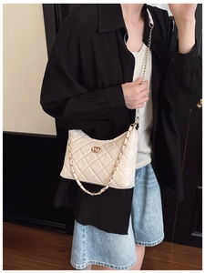 Close-up of beige quilted shoulder bag with metal chain strap and double ring buckle