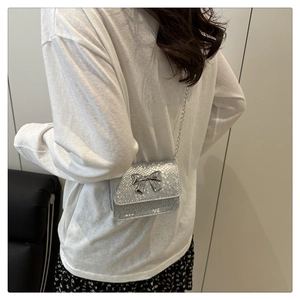 Silver mini crossbody bag with snakeskin texture and metal bow detail on a model