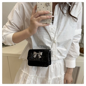 Detail of a black snakeskin embossed crossbody bag with a silver metal bow buckle detail