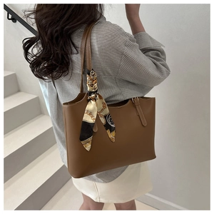 Brown leather tote bag with a decorative silk scarf held by a model on white stairs