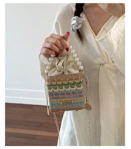 Detail of woven straw bucket bag with white pearl handle and golden chain strap