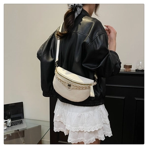 Detailed view of white saddle bag with embossed texture and gold chain worn by model