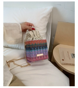 Detail of colorful woven bucket bag featuring pearl handle and gold chain strap on white bed