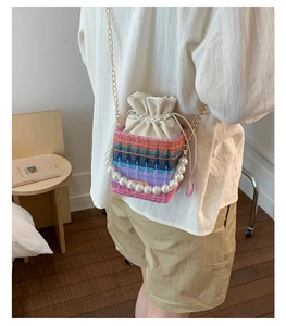 Detailed shot of a woven bucket bag with pearl handle and golden chain strap