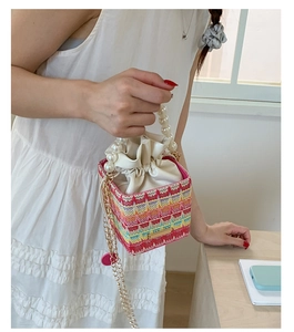 Detailed shot of a woven bucket bag with pearl handle and golden chain on a white dress