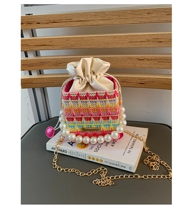 Detail of colorful woven mini bucket bag with pearl handle and golden chain strap