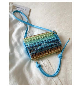 Detail of multi-colored gradient straw crossbody bag featuring gold hardware and blue straps