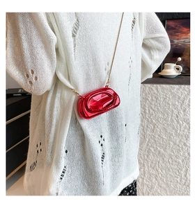 Glossy red acrylic mini evening clutch bag with golden chain worn over white knitwear
