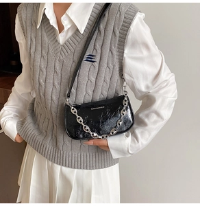 Dettaglio della borsa a spalla nera lucida con catena d'argento su abbigliamento moda