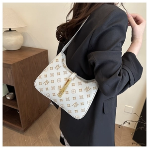 Close-up of a vintage monogram shoulder bag with gold clasp on a model in a black blazer