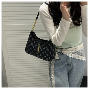 Detail of black monogram shoulder bag with gold chain strap worn by a model