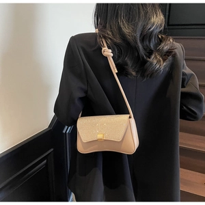 Détail du rabat scintillant et boucle dorée sur un sac à bandoulière beige chic