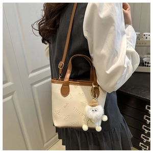 Détail du mini sac seau avec motifs embossés et un pendentif poupée en peluche blanche