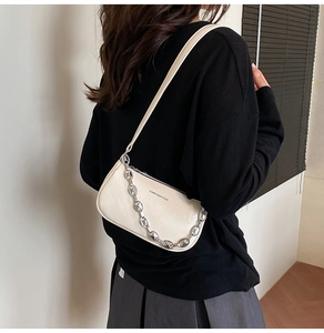 Dettaglio di borsa sottobraccio in pelle bianca con catena d'argento indossata da modella