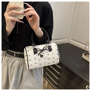 Détail du sac Boston blanc avec imprimés nœuds noirs et pendentif en métal en cœur