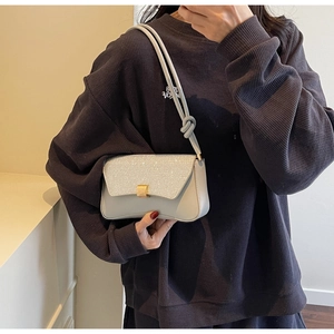 Détail d'un sac baguette gris clair avec rabat à paillettes argentées et fermoir doré