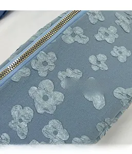 Detailed macro view of 3D floral texture and metal zipper on a blue canvas bag