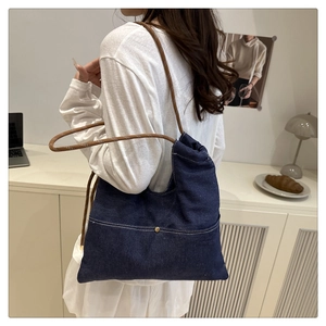 Close-up of deep blue denim tote with brown braided rope straps and golden rivet detail