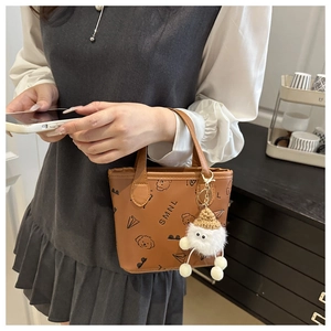 Détail d'un mini sac seau marron en cuir PU avec motifs et pendentif en peluche blanche