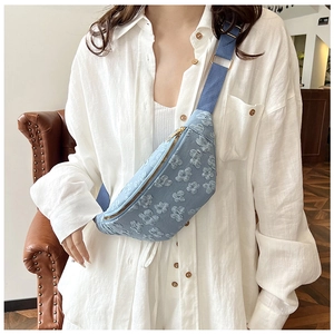 Close-up of light blue floral embroidery on a saddle bag with golden zipper details