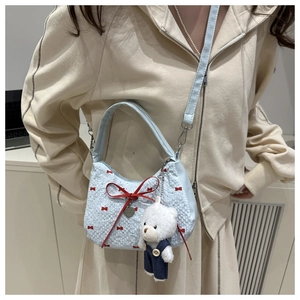 Detail of light blue crescent bag with red bows and white plush bear pendant charm